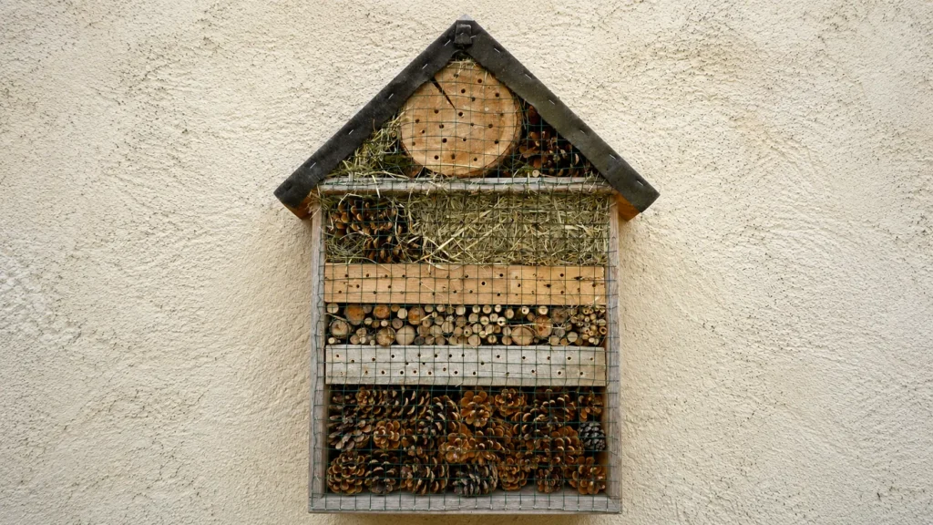 Insektenhotel mit Tannenzapfen, Heu, Holzscheiben und verschiedenen Füllmaterialien